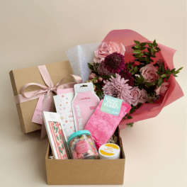 Pink flower bouquet beside a gift box filled with small packaged items