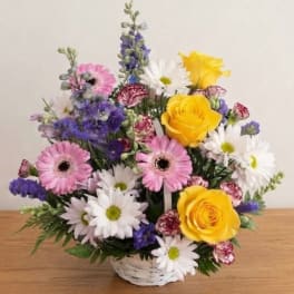 Mixed bouquet of yellow roses, pink gerberas, and white daisies in a white basket