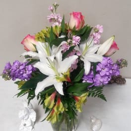 Bouquet of white lilies, pink roses, and purple flowers in a glass vase