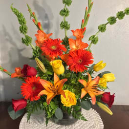Mixed bouquet with red and yellow roses, orange lilies, and gerbera daisies in a vase