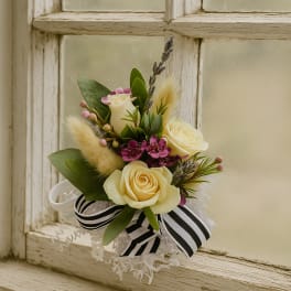 Small floral arrangement with cream roses, purple accents, and a black-and-white ribbon