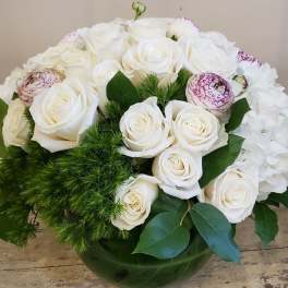 White roses and hydrangeas in a green glass vase with greenery