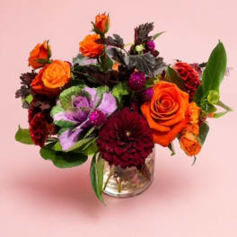 Orange and burgundy flower arrangement in a clear glass vase