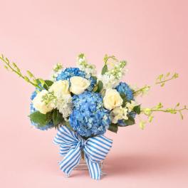 Blue hydrangea and white rose bouquet in a glass vase with a striped ribbon