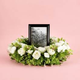 White floral wreath around a framed black-and-white photo on a pink background