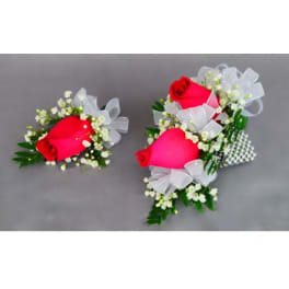 Two rose corsages with white ribbon bows on a gray background