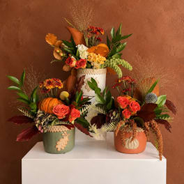 Three autumn floral arrangements in decorative pots on a white pedestal.