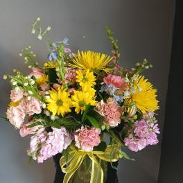Mixed bouquet of yellow daisies and pink flowers in a glass vase with ribbon