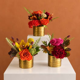 Three floral arrangements in gold containers on white pedestals