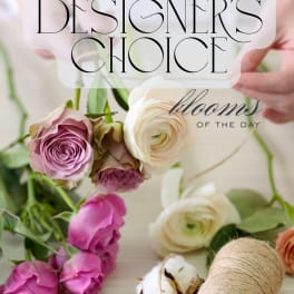 Florist arranging pink and cream roses and ranunculus with twine on a light table.