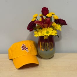 Mixed bouquet in a red vase beside a yellow baseball cap