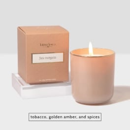 Lit peach scented candle beside its box on a white tray