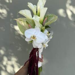 White calla lilies and orchids in a hand-tied bouquet with burgundy trailing accents