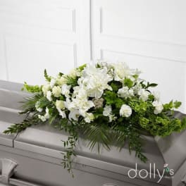 White floral casket spray with green accents on a gray casket