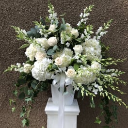 White floral arrangement in a white pedestal vase with a ribbon bow