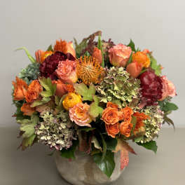 Low ceramic vase of orange and peach roses, hydrangeas, and mixed warm-toned flowers