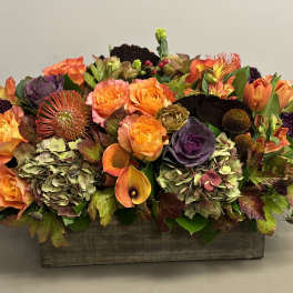 Low centerpiece of orange roses and mixed autumn flowers in a rustic wooden box.
