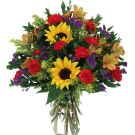 Bouquet of sunflowers, red carnations, and purple accents in a glass vase