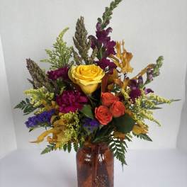 Mixed bouquet of roses and fall flowers in an amber glass vase