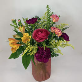 Mixed bouquet in a pink glass vase with bright pink, yellow, and purple flowers