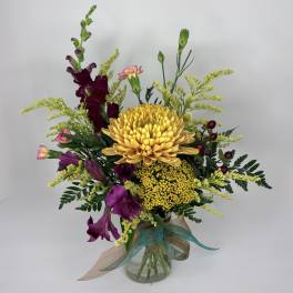 Mixed bouquet of yellow and purple flowers in a glass vase with ribbon