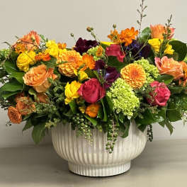 Low centerpiece of bright roses, dahlias, and green hydrangeas in a white ceramic bowl