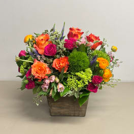 Mixed bouquet of orange, pink, and yellow flowers in a wooden container