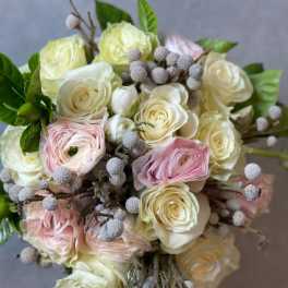 Round bouquet of cream roses, blush ranunculus, and gray berries in a tight clustered design