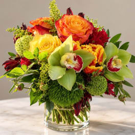 Mixed bouquet of orange and yellow roses with green orchids in a glass vase