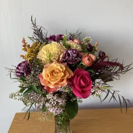 Mixed bouquet of roses, chrysanthemums, and small filler flowers in a glass vase