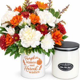 Bouquet of orange, white, and red mums in a white mug beside a candle jar