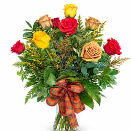 Bouquet of red, yellow, and tan roses in a glass vase with a plaid ribbon