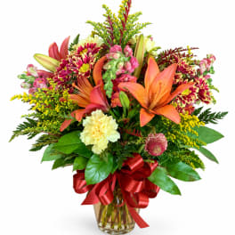 Mixed bouquet of lilies, chrysanthemums, and carnations in a glass vase with a red ribbon