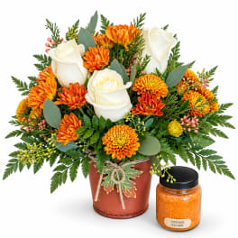 Orange and white flower arrangement in a metal pot with a candle jar beside it