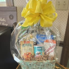 Gift basket with assorted snacks wrapped in clear cellophane and topped with a yellow bow