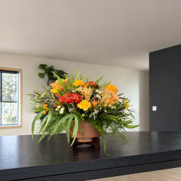 Mixed orange, yellow, and red flowers arranged in a low bowl on a stand