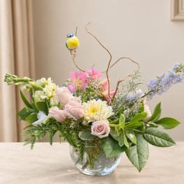 Pastel flower arrangement in a clear glass vase with a small bird ornament