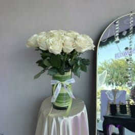 Tall bouquet of white roses in a green-lined glass vase tied with ribbon