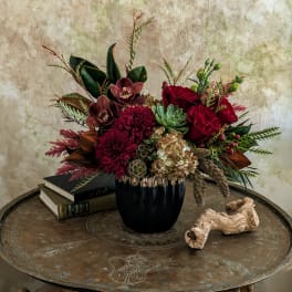 Red and burgundy floral arrangement in a black vase on a table