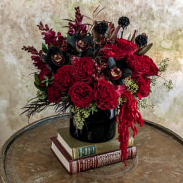Red rose arrangement in a black vase with dark accent flowers