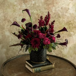 Dark burgundy floral arrangement in a black patterned vase on stacked books