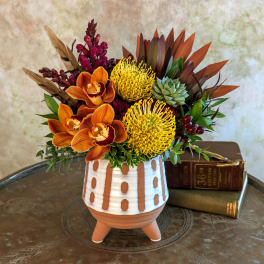 Orange orchids and yellow pincushion blooms in a patterned ceramic pot