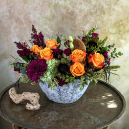 Orange roses and purple flowers arranged in a white bowl vase