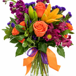 Bouquet of orange roses, yellow lilies, and purple flowers in a glass vase