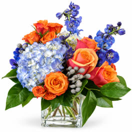 Orange roses and blue hydrangeas in a clear glass vase