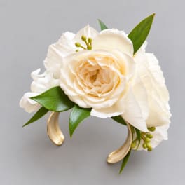 White floral corsage with cream rose and green leaves on a gold bracelet