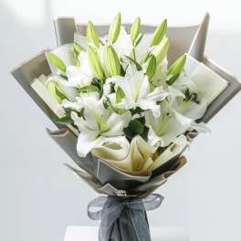 Bouquet of white lilies wrapped in gray paper with a ribbon