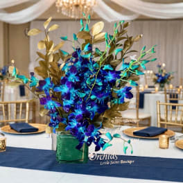 Blue orchid centerpiece in a green glass vase with gold foliage