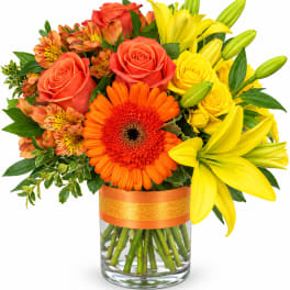 Bright mixed bouquet of roses, lilies, and gerbera daisies in a glass vase