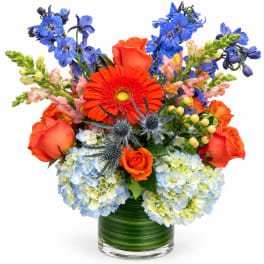 Bright mixed bouquet in a glass vase with orange, blue, and pale blooms